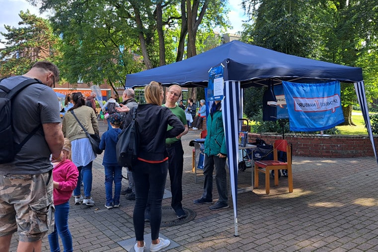 Sprachbrücke-Hamburg e.V. beim Fest zum Weltkindertag in Eidelstedt. Auf dem Foto: Der Vereinsstand, davor mehrere interessierte Besuchende. 